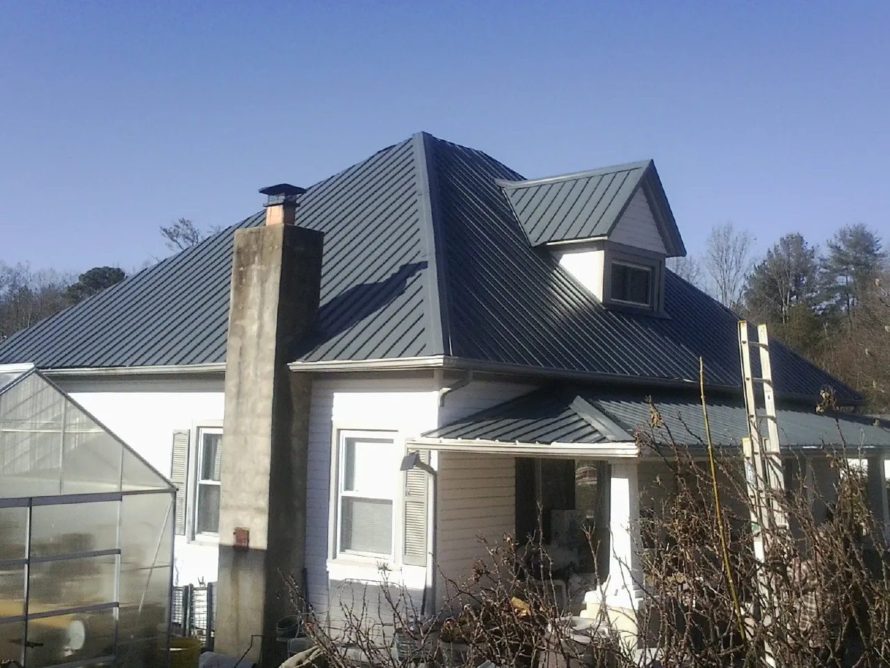 Dark blue standing seam metal roof on a white farmhouse with dormer — Slate & Tile Roof Repair by Roofing Brothers in Yatesboro