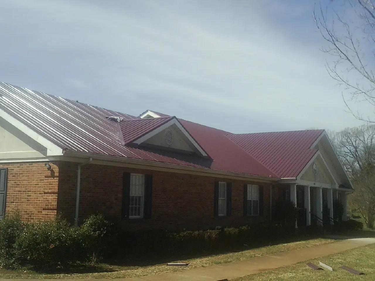 Red metal roof with gabled entries on a long brick building, from a Hail Damage Roof Repair job in Yatesboro