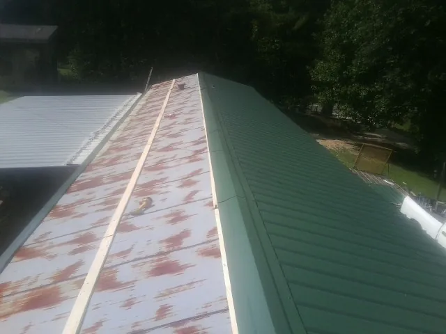 Old rusted panels beside newly installed green metal roofing — Wind Damage Roof Repair by Roofing Brothers in Yatesboro