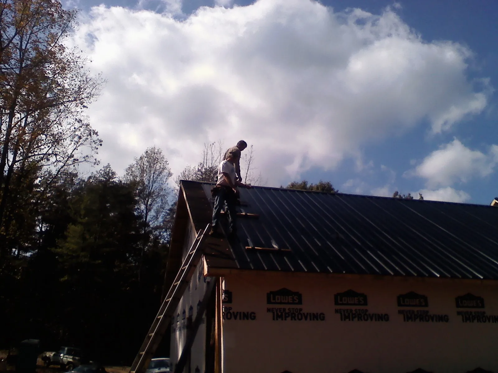 Roofer fastening dark metal panels high against a cloudy sky, from a Roof Inspection job in Yatesboro