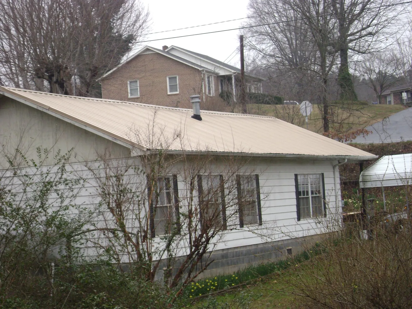 Tan metal roof on a white sided house set into a hillside — Commercial Roofing by Roofing Brothers in Yatesboro