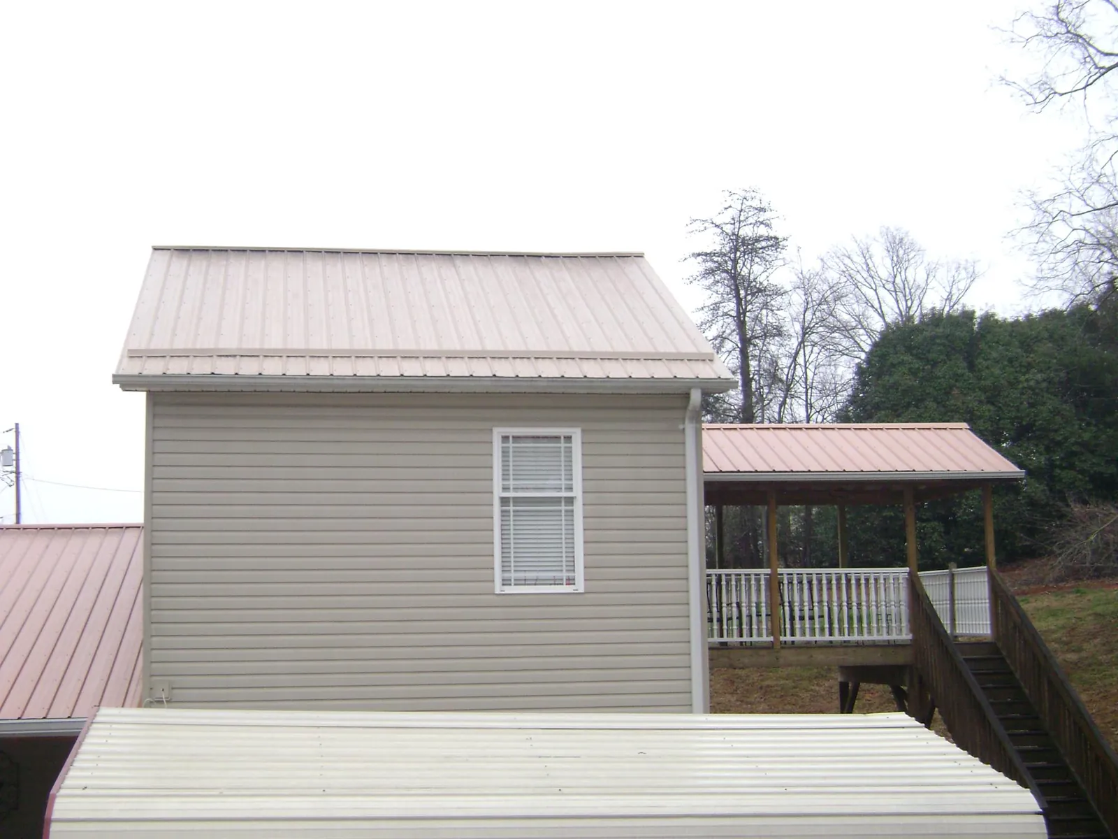Tan metal roofs on a two story addition and attached porch, from a Roof Replacement job in Yatesboro